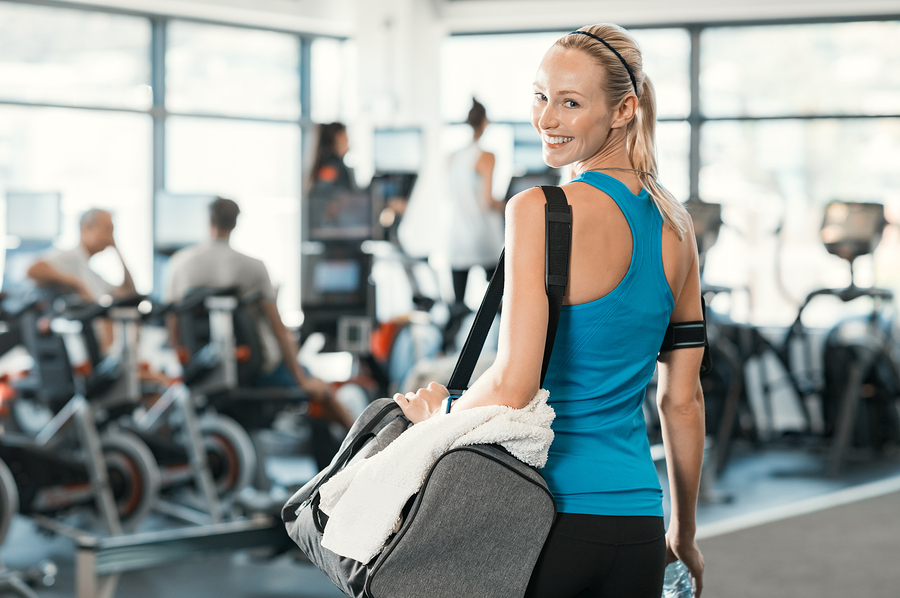 Fit woman holding gym bag in a fitness centre. Beautiful blonde woman ready to start her training. Portrait of energetic woman looking at camera ready for new inscription at the gym.