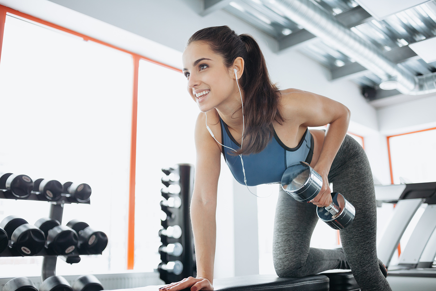 Young beautiful woman doing exercises with dumbbell in gym. Glad smiling girl is enjoying with her training process. She is working hard